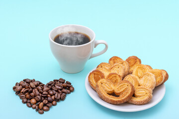 Steaming coffee cup, heart shaped cookies, heart shaped coffee beans on a blue background. Morning breakfast