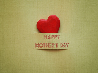 Happy Mothers day with a red wooden heart shape on a green paper background