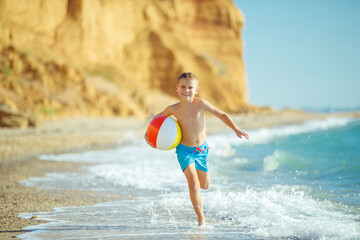 Boy child has fun at sea. Summer, happiness, sea and a child with a ball. High quality photo.