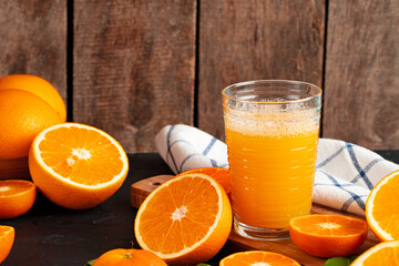 Glass of orange juice and cut oranges on table