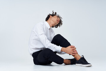 man with curly hair in a classic suit and sneakers sits on the floor and side view Copy Space