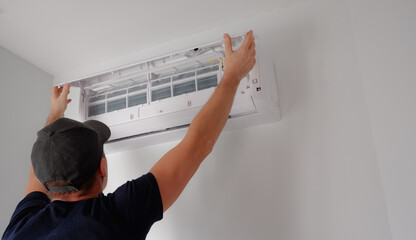 Air conditioner repair and maintenance. The technician removes the filter of the indoor unit for...