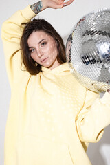 Naklejka premium Close up portrait of young and sensual woman in yellow hoodie holding disco ball.