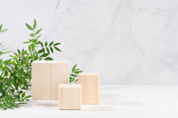 Wooden square podiums with green branch of tree in sunlight on white wood table, marble wall. Fashion showcase for cosmetic products, goods, shoes, bags, watches.