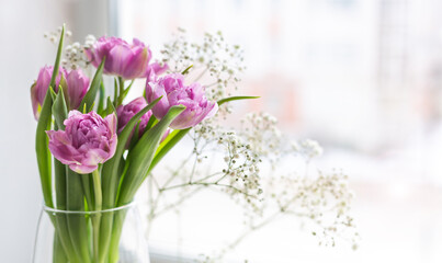 Romantic delicate bouquet of pink tulips and Gypsophila in a glass vase by the window. Greeting card for mother's day, March 8 or wedding. Floristics, flower shop. The freshness of a spring morning.