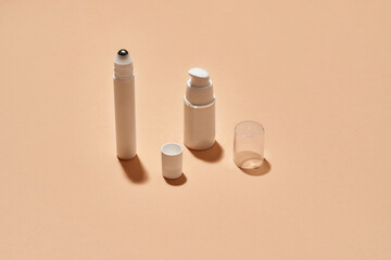 White plastic pump bottle and tube for eye roller skin care product isolated over beige background with reflection