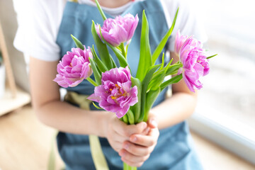 A bouquet of beautiful pink tulips in the hands of a girl in a blue apron. The concept of growing flowers, gardening and floristry. Flower shop. Spring interior decor. Give with love.