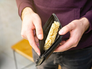 Noodles in the wallet in young man hands. Instant noodle (ramen) in pocket in men's hand as poverty...