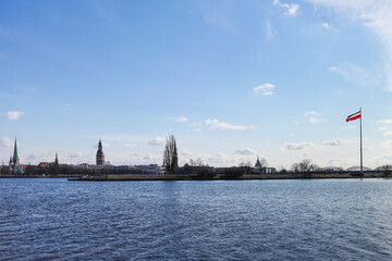 City view of the Old Town of Riga from the other side of the Daugava River with the national flag of the Republic of Latvia