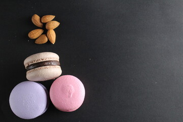 the layout top three macaroons and almond nuts lie on a black background with room for text and with a copyspace