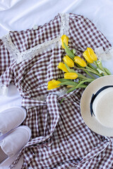 Woman clothes flat lay with cute plaid dress, straw hat, gray shoes and bouquet of yellow tulips, female trendy set of minimalistic apparel, content for fashion blogger, girlish style