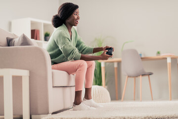 Profile side view of attractive cheerful girl sitting on divan playing game having fun hobby at house flat indoor living-room