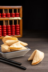 Close-up of chopsticks, fortune cookies on saucer, on dark wooden table with abacus, selective...