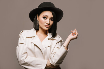 Pretty young woman in white coat and hat posing on brown background