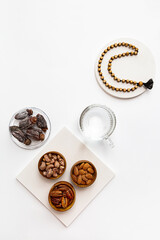 Ramadan Kareem and iftar muslim food, modern holiday concept. Wooden bowls with nuts and dried fruits and the moon made of beads for rosary with tassel on a white background with copy space