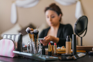 Lipsticks and makeup brushes on a wooden table, in the background a woman putting on makeup