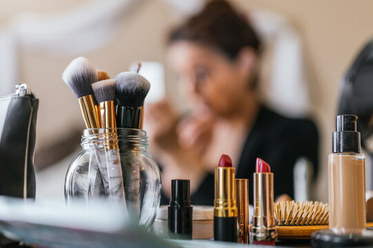 Lipsticks on a wooden table and in the background a woman putting on makeup