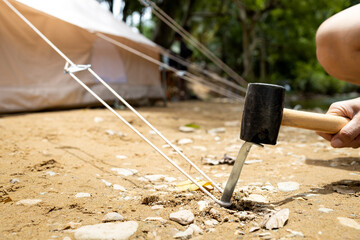 Hand of male holding a rubber mallet,hammering aluminium steel tent stakes pegs nail,fastening tent...