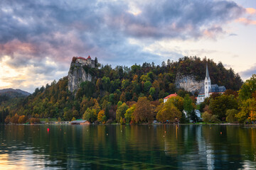 Fototapeta na wymiar Scenic view of the Bled castle on the cliff at sunset, Bled lake (Blejsko jezero) in Slovenia, amazing autumn landscape with colored sky. Outdoor travel background