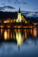 Fototapeta na wymiar Famous alpine Bled lake (Blejsko jezero) in Slovenia, amazing night landscape. Scenic view of the lake, island with church in lights, mountains and blue sky with clouds, outdoor travel background