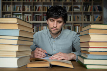 Man student sits at a table in the library, littered with books.