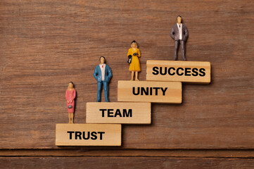 People miniatures standing on wooden blocks written with TRUST, TEAM, UNITY and SUCCESS