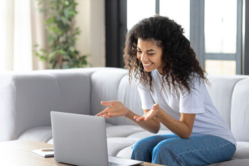 Young successful african american woman sitting at home on the couch streaming something on a laptop