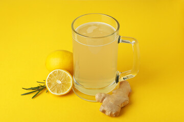 Glass of ginger beer and ingredients on yellow background