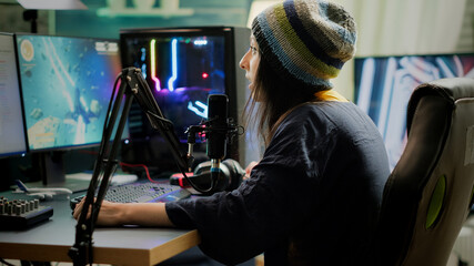 Cyber woman streamer looking at camera and smiling while streaming chat is open. Videogamer streamer playing space shooter video game at gaming home studio equipped with professional equipment