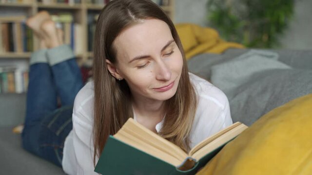 Close up woman lying on a comfortable couch and reading an exciting book