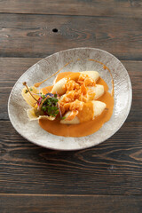 Delicious seafood with orange sauce on plate on table, three potato cutlets served with vegetables and sprouts in cheese basket. From above view of shrimps cooked in restaurant for dinner.