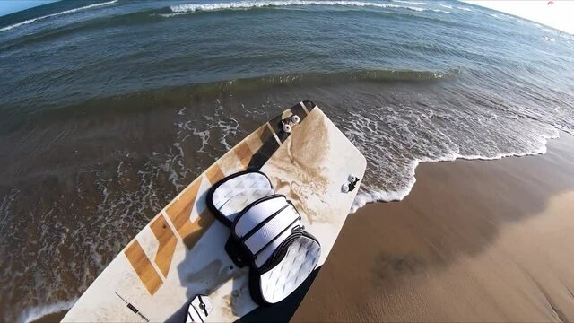 POV man picks up kitesurfing board sand runs into water jump sunny summer day