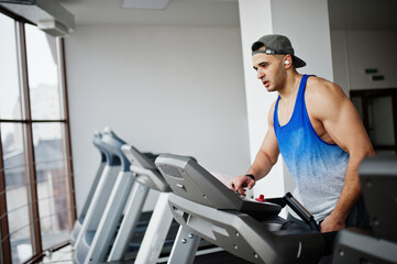 Fit and muscular arabian man running on treadmill in gym.