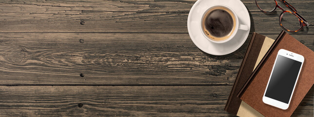 アンティークなテーブルの上にあるコーヒーと本、眼鏡、スマートフォン。真上からのアングル