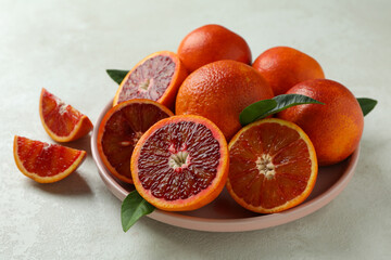 Plate with red oranges and leaves on white textured background