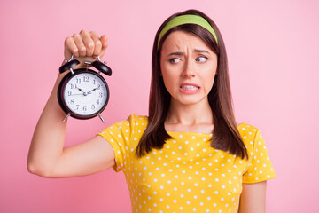Photo of young beautiful unsure uncertain doubtful girl hold and look at clock isolated on pink...