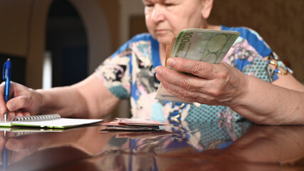 Fototapeta na wymiar Woman counting cash and writing down budget. Elderly pensioner makes savings.