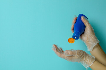 Female hands in gloves hold sunscreen on blue background