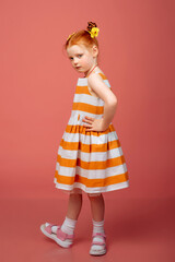 A little girl with red hair plays, spins and dances on a pink background.