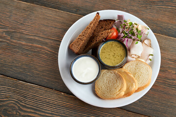 Top view of white and dark bread slices serves with sprouts, vegetables and pork fat on plate. Tasty snack with sour cream and green sauce in restaurant. Concept of traditional ukrainian cuisine.