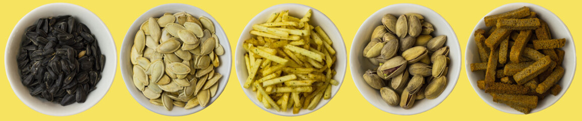 Snacks on a yellow background. View from above. Pistachios, pumpkin seeds, sunflower seeds, crackers, fried potatoes