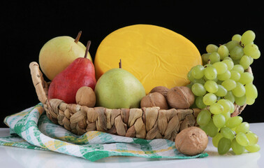 Large round head of cheese in a yellow package in a wicker basket with nuts,honey and fruit close-up.
