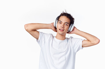 happy curly-haired guy in headphones and in a white t-shirt listens to music and holds his hands near his face