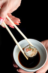 A woman's manicured hands hold wooden sticks of a classic salmon roll on a black background. Space for text, flatlay