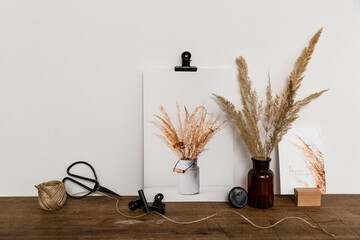 Arrangement von Bürozubehör und Fotos als Fine Art Print und Postkarte mit Pampasgras, Holz und Metallklammern auf einem rustikalen Holztisch