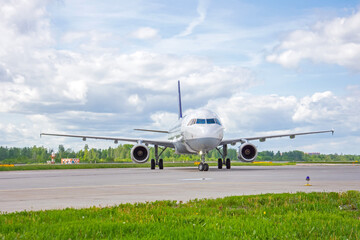 Airplane on airport taxiway bright green grass and scenic blue sky with clouds.