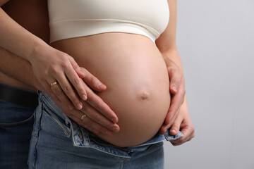 Man touching his pregnant wife's belly on light background, closeup