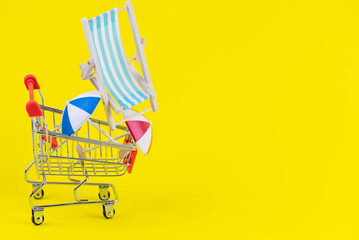 Vacation travel tour sale concept. Tourism opening. Sun lounger and summer umbrella in a shopping cart on trendy yellow background.