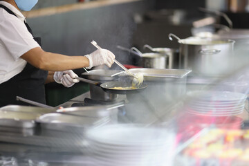Cook prepares food in frying pan in kitchen
