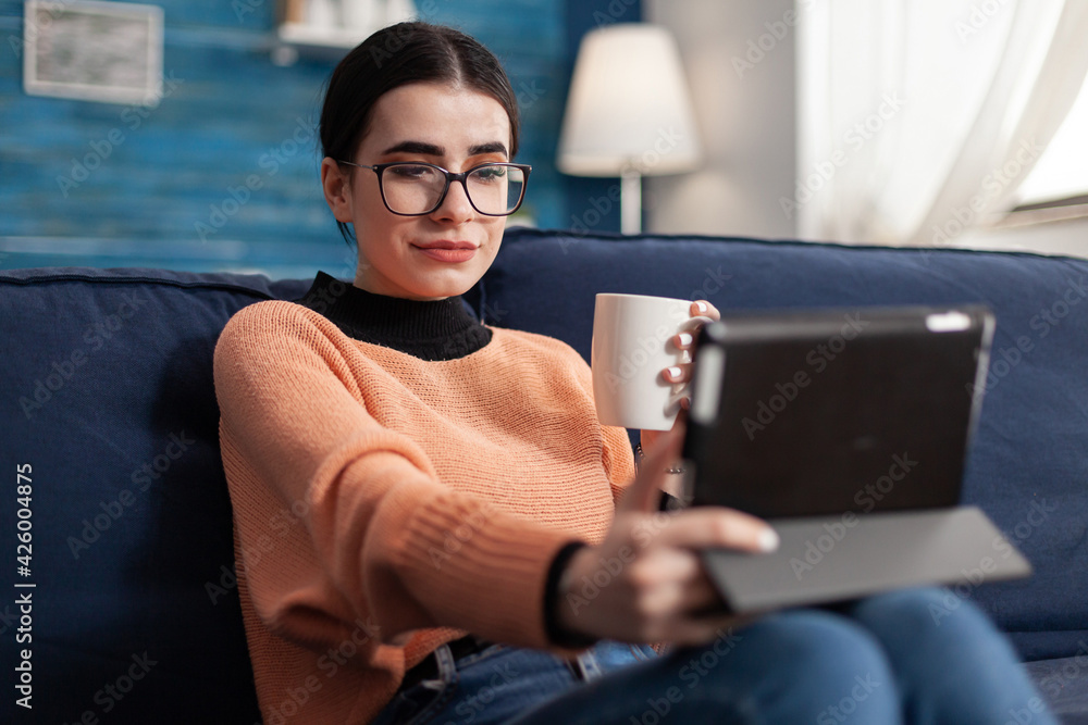 Poster student reading online book on digital application using tablet computer, sitting on sofa in living 